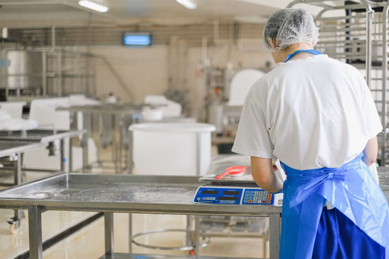 A food-production worker wearing a hair covering and apron at a digital scale