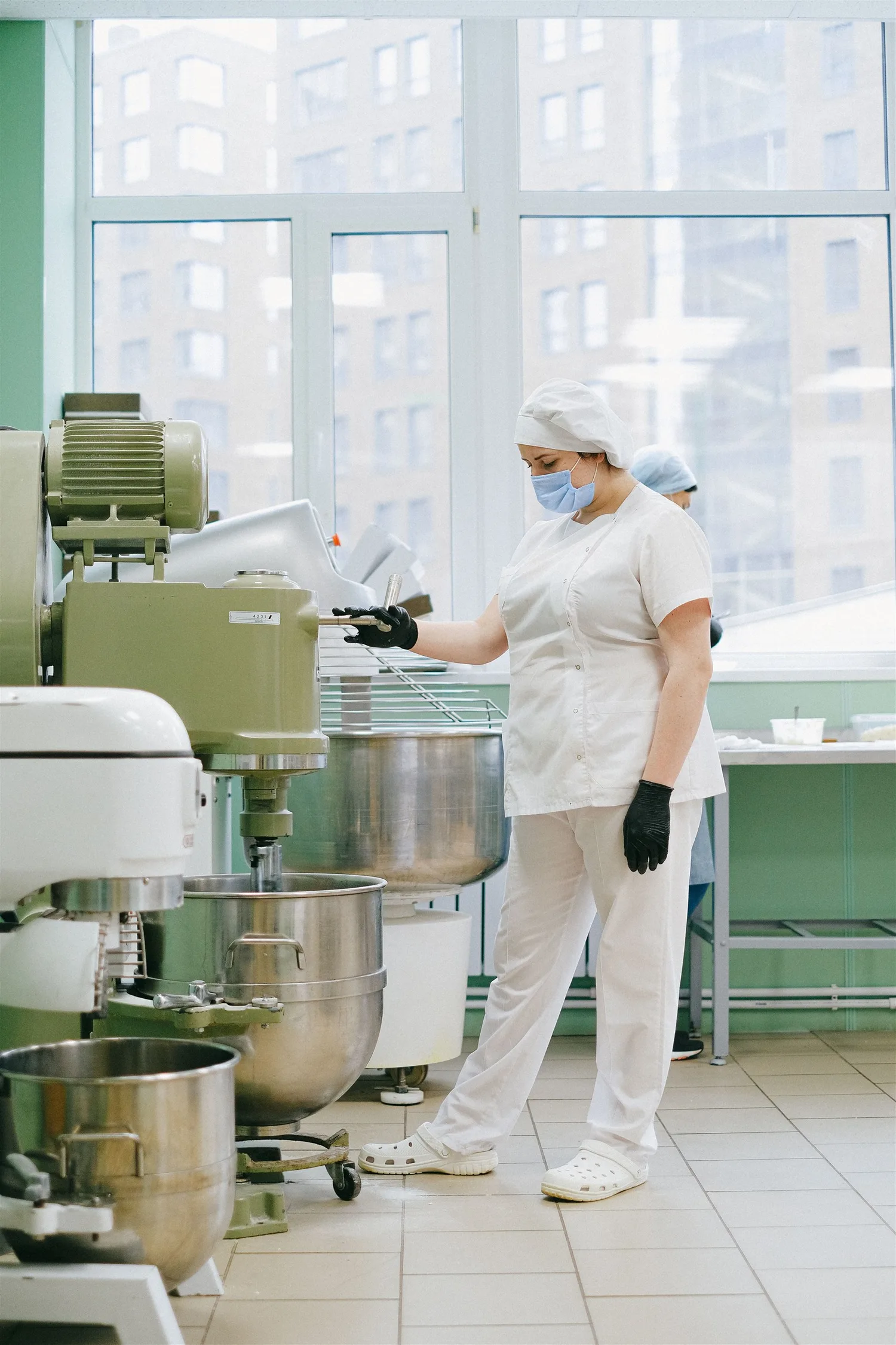 A food-production worker in protective clothing using an industrial mixer